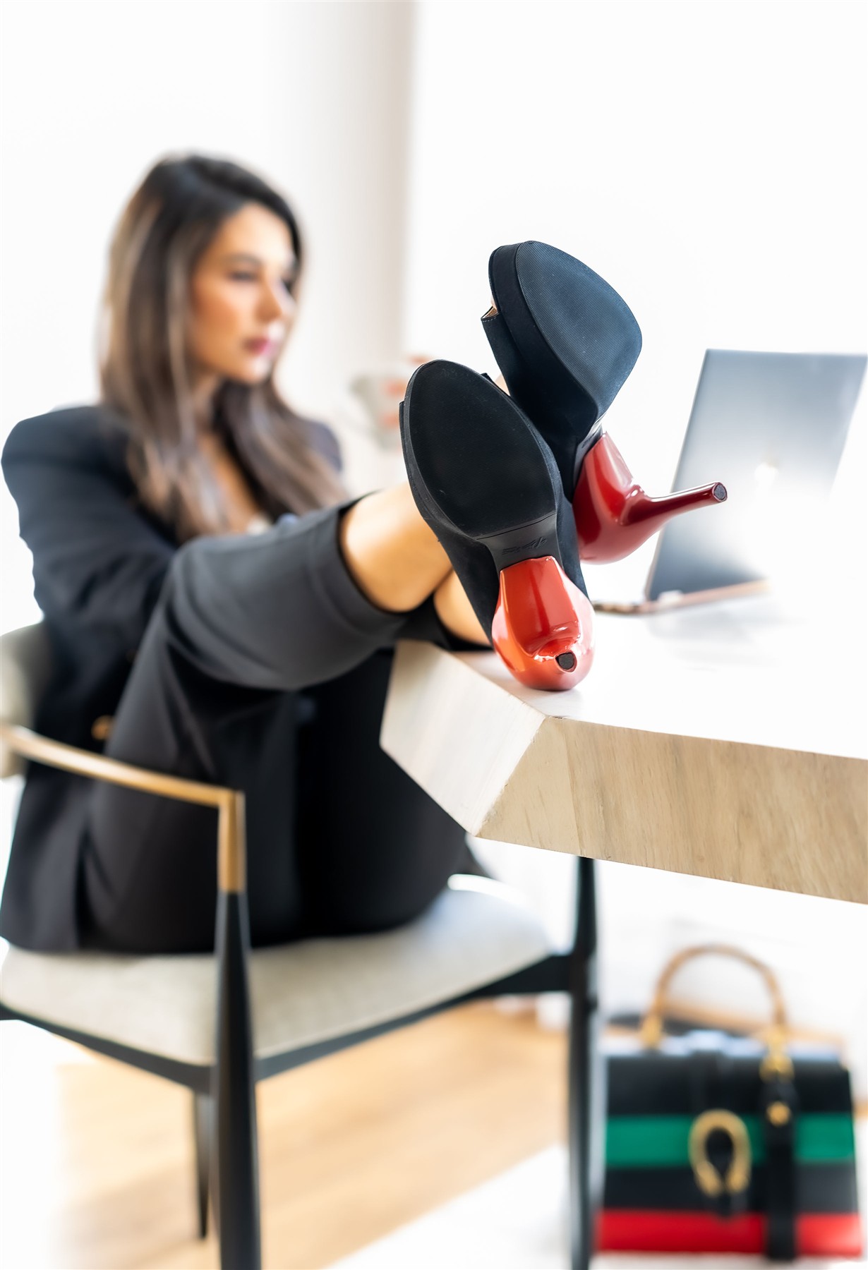Model in a black outfit styling black slim high heels with red heel covers at a desk